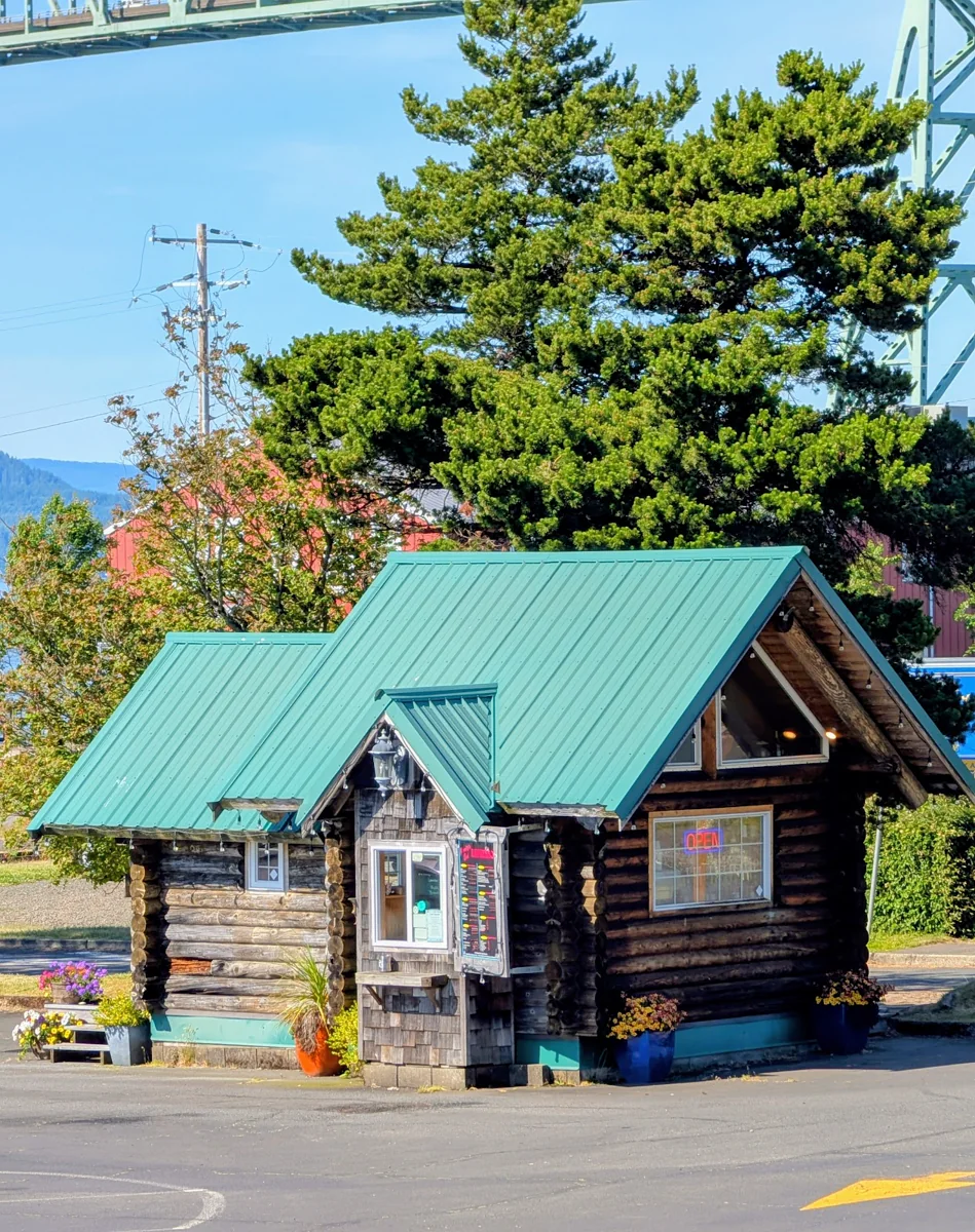 The log-built Journey's End Espresso kiosk with its service window, menus, planters, and nearby bridge